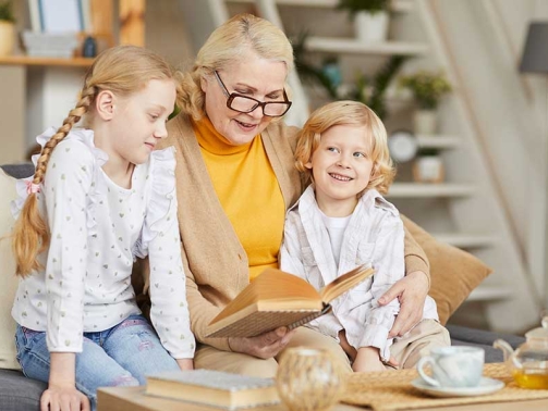 A woman wearing glasses readying a book to two children