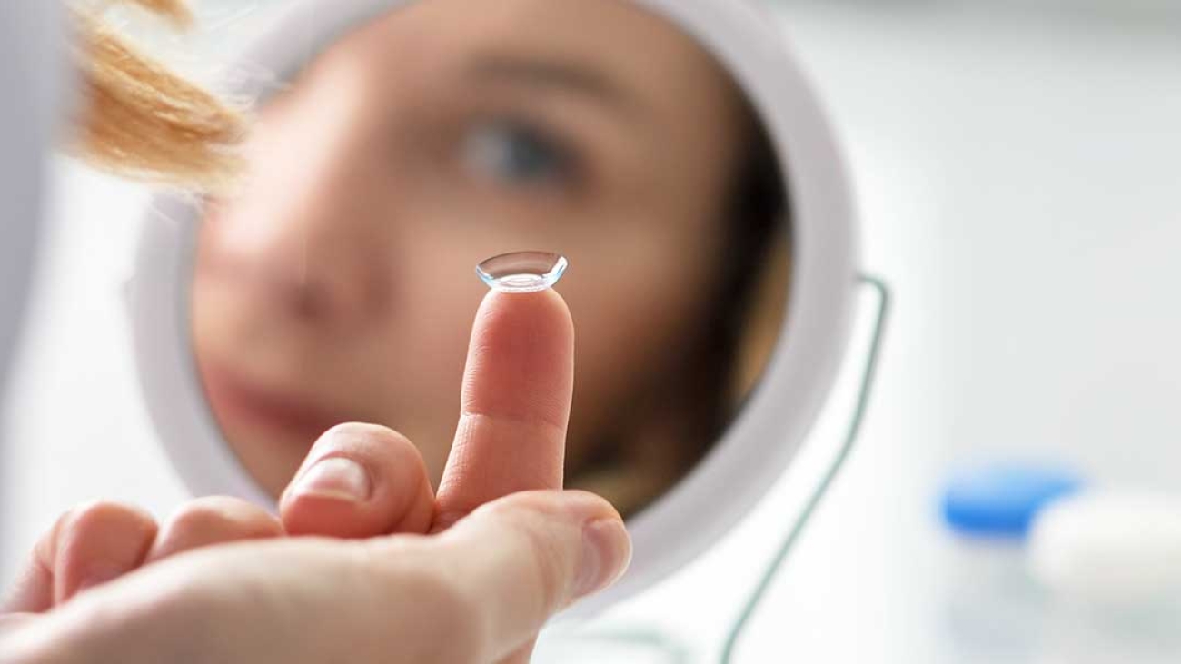 Woman using a mirror to put in a contact lense