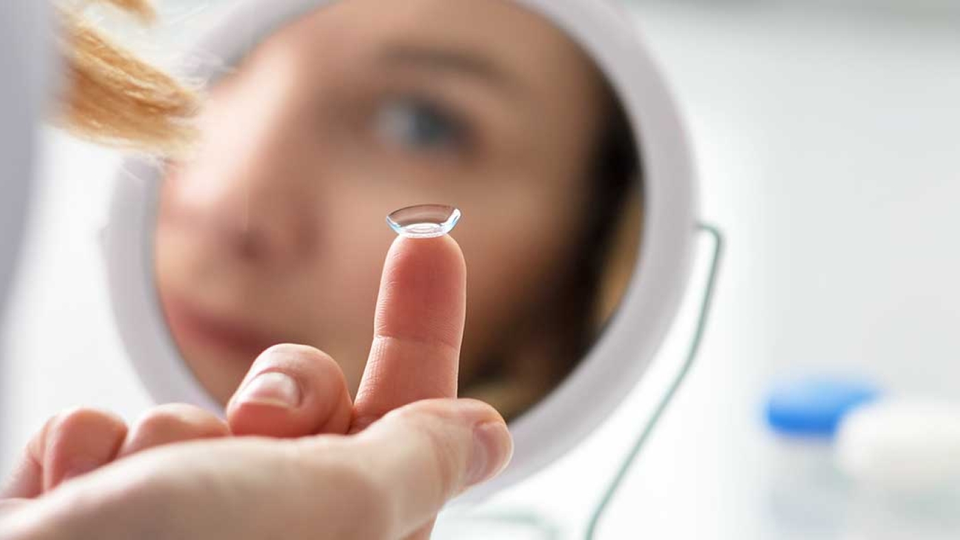 Woman using a mirror to put in a contact lense